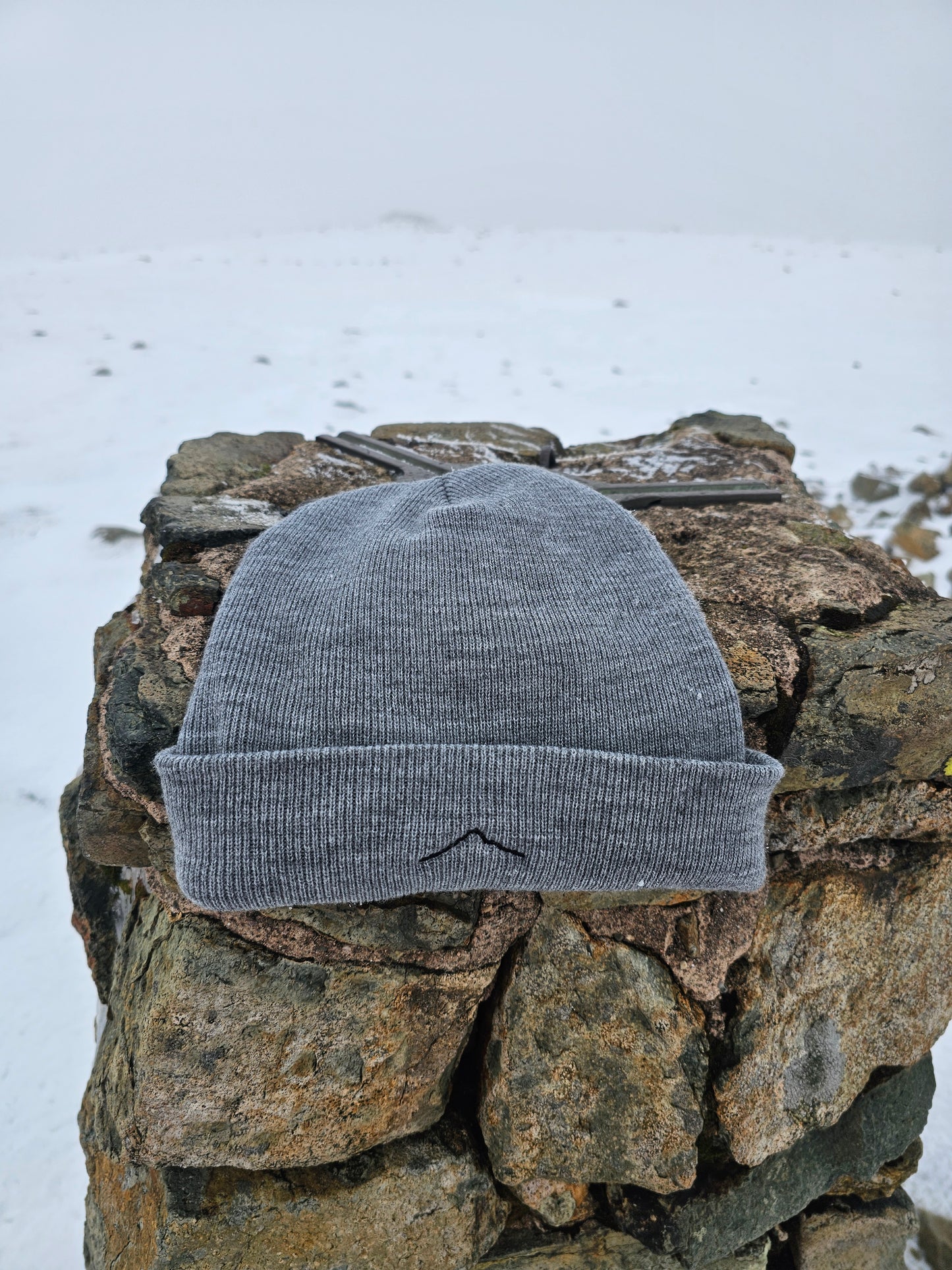 Gray knit beanie on a stone surface with snow in the background