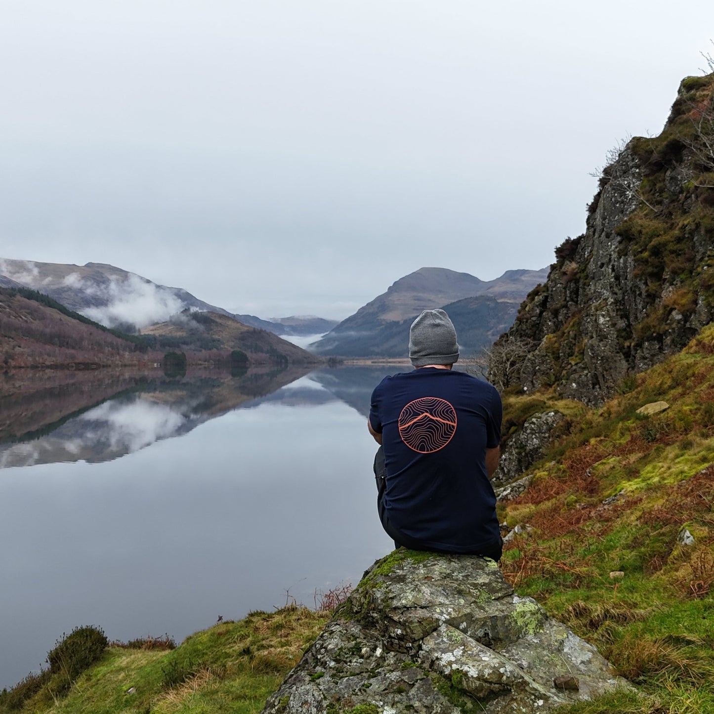 Person sitting on a rock overlooking a lake with mountains in the background
