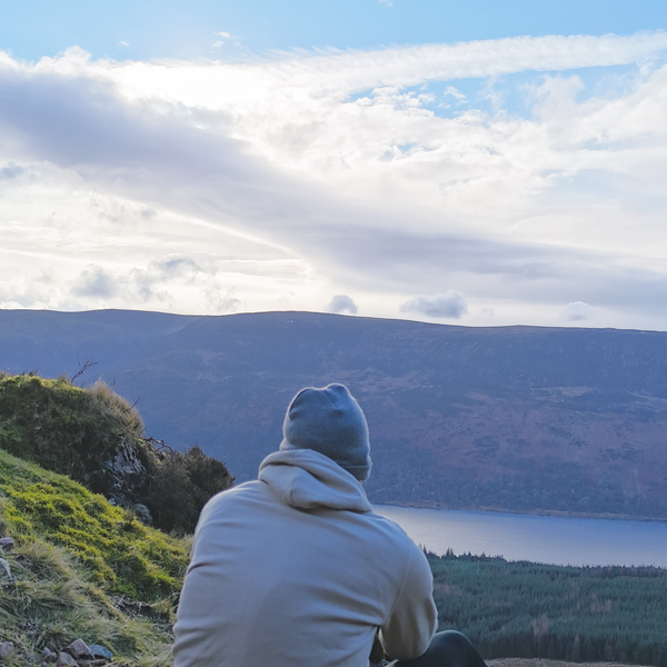 Person sitting on a grassy hill overlooking a lake with mountains in the background