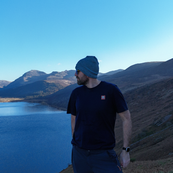 Person standing on a hill overlooking a lake with mountains in the background