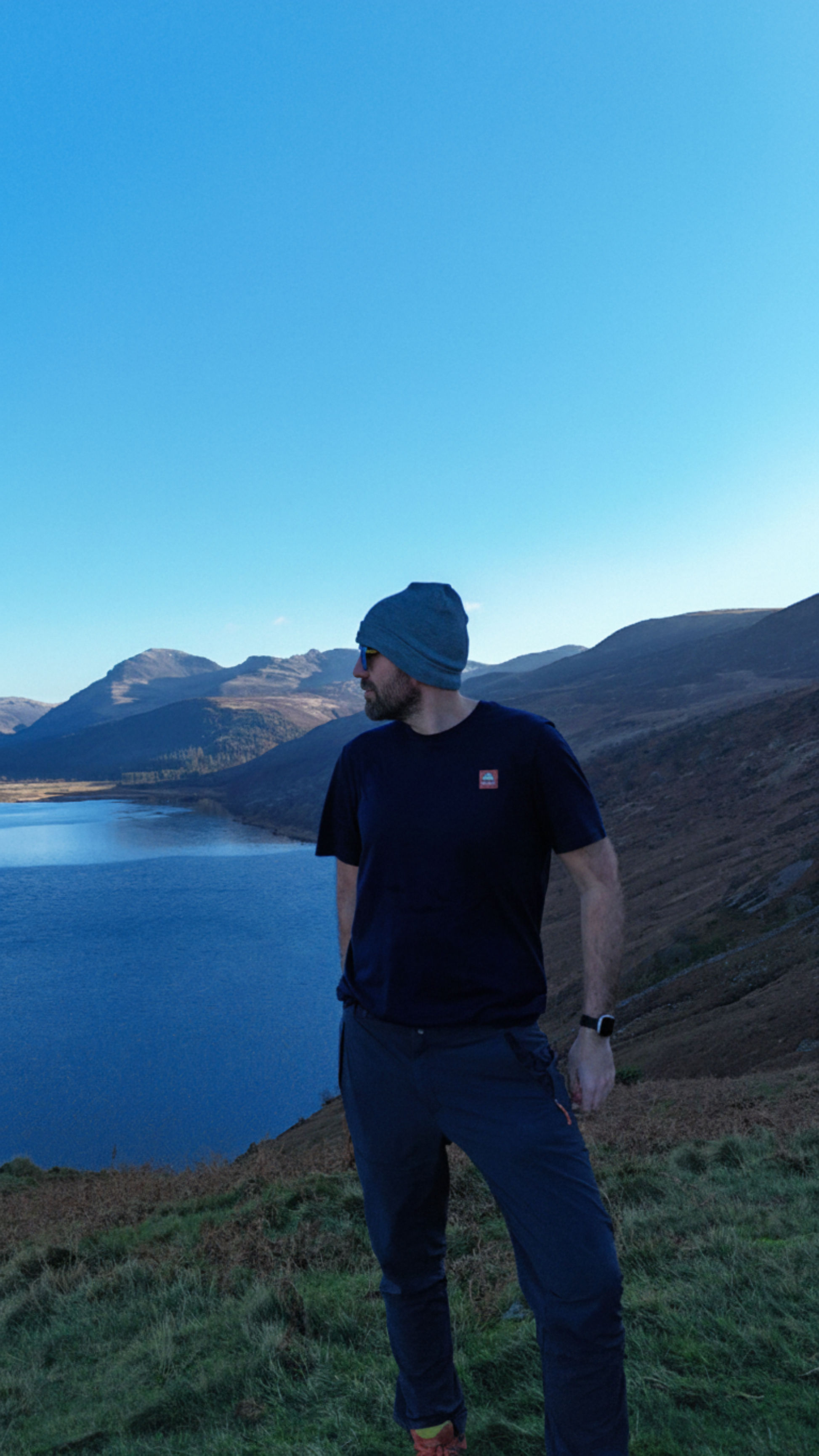 Person standing on a hill overlooking a lake with mountains in the background