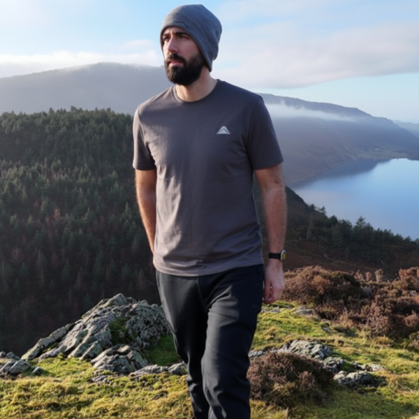 Man standing on a mountain with a scenic view of a lake and trees.