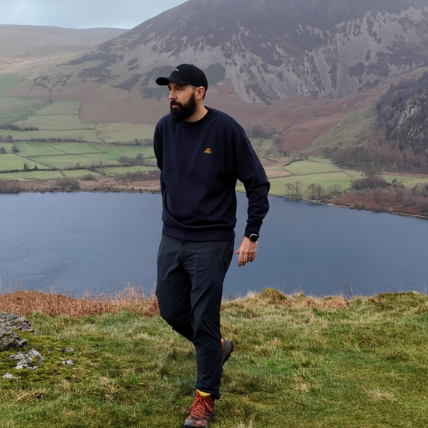 Man walking on a grassy hill with a lake and mountains in the background